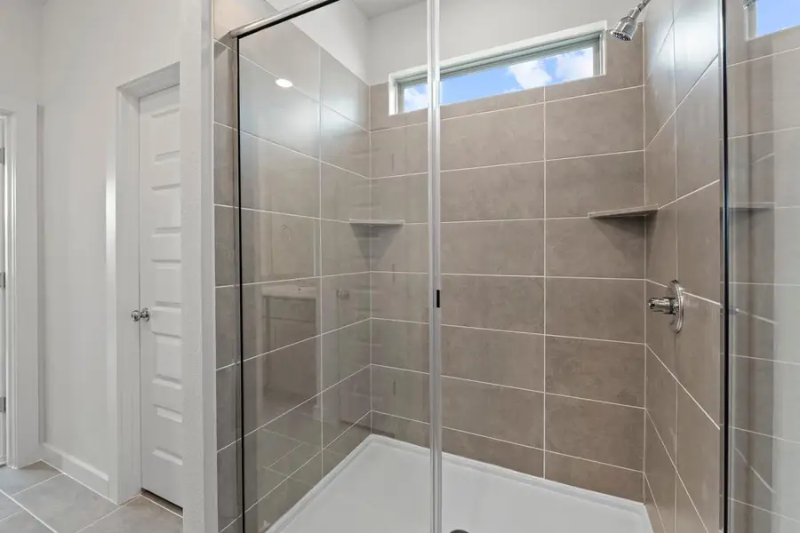 A spacious, glass-enclosed shower stall features sleek tile walls and a high window for natural illumination. A spacious, glass-enclosed shower stall features sleek tile walls and a high window for natural illumination.