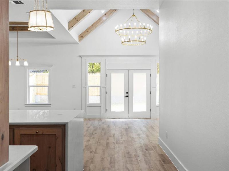 Entrance foyer with beamed ceiling, light wood finished floors, a chandelier, french doors, and high vaulted ceiling