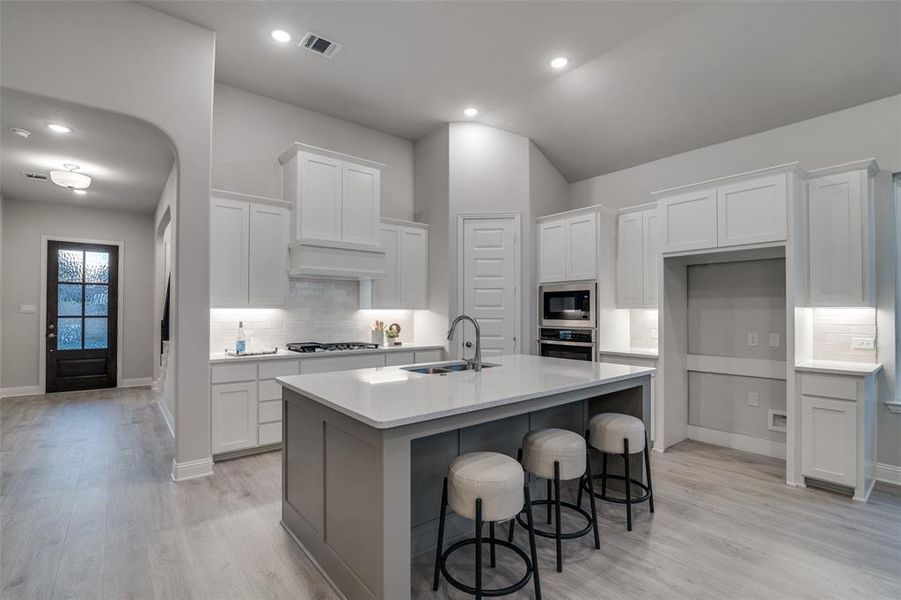 Kitchen with built in microwave, white cabinetry, a center island with sink, and sink