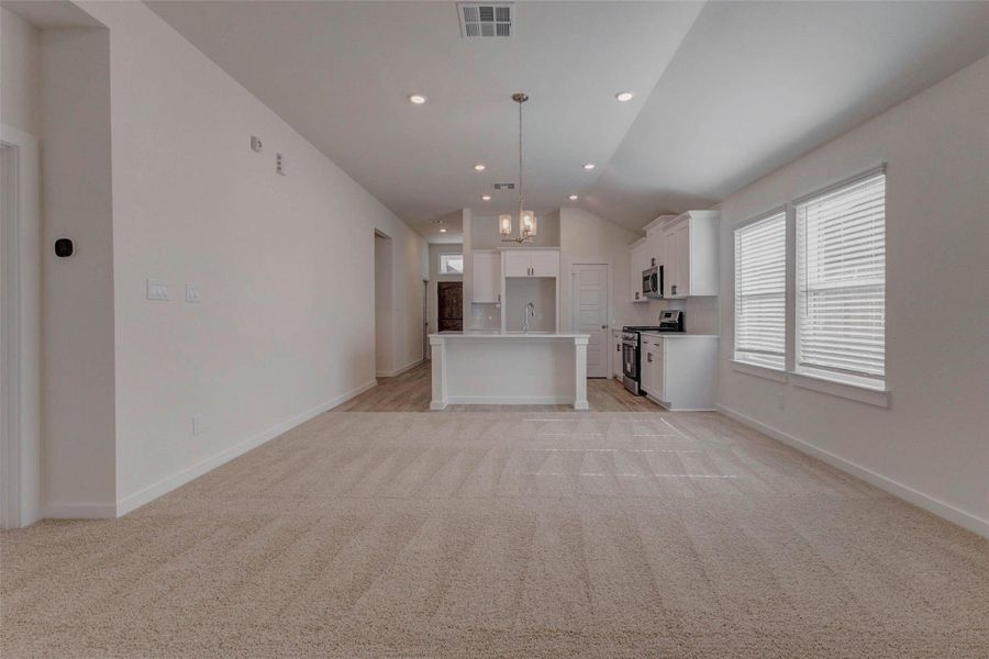 This stunning open-concept space seamlessly connects the kitchen and living areas with expansive sightlines, soft neutral tones, and large windows that draw in natural light. Vaulted ceilings with recessed lighting add volume, while plush carpeting transitions effortlessly into wood-look tile, creating the perfect blend of comfort and style.