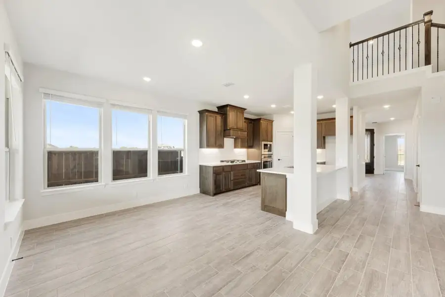 Open-concept living area and kitchen with dark wood cabinets, light tile floors, and a second-floor overlook railing.