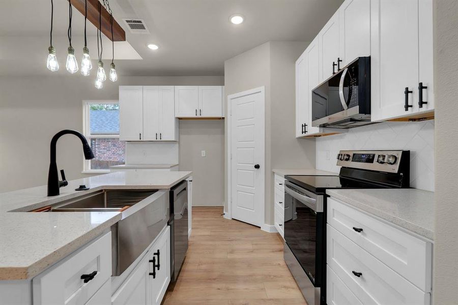 Kitchen with light wood-type flooring, decorative light fixtures, light stone countertops, stainless steel appliances, and white cabinetry