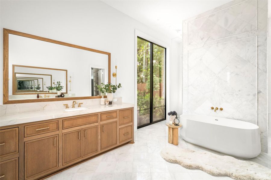 The spa-like primary bath features dual vanities finished in quartzite and custom cabinetry. Along with soaking tub, a full diamond patterned marble wall, and large walk-in shower.