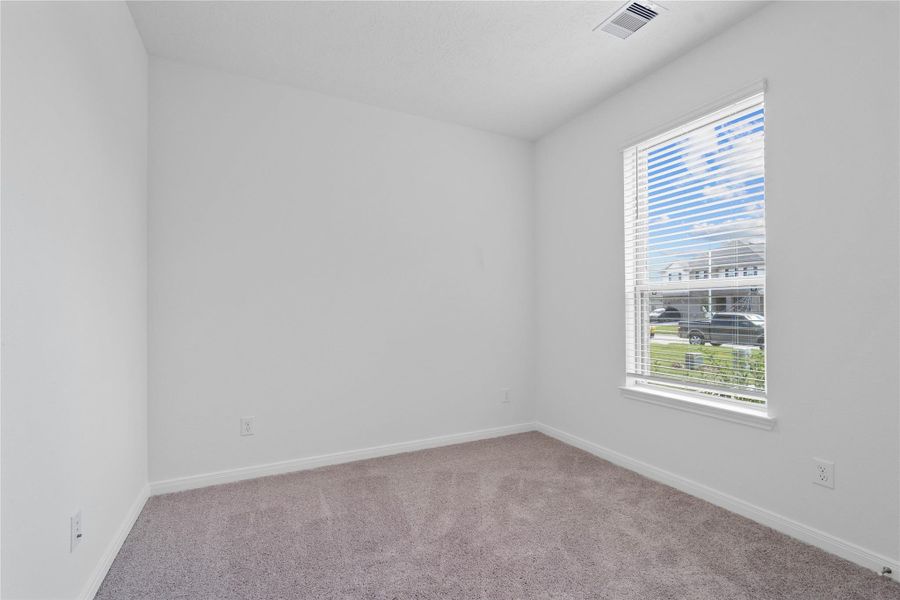 Tucked peacefully in the front of this home is this secondary bedroom. It offers comfort and style with plush carpeting, neutral paint tones, recessed lighting, a large window with blinds, and a generously sized closet.