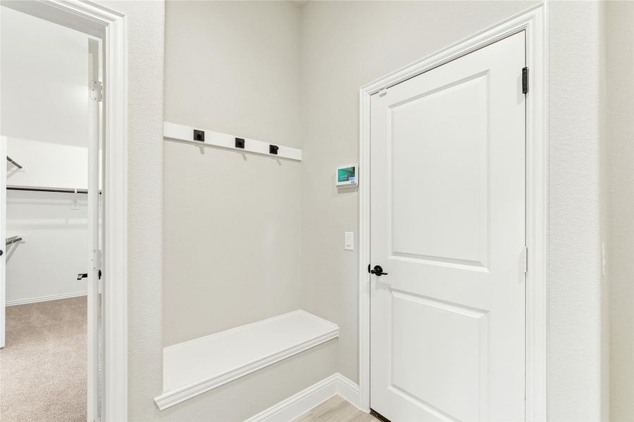 Mudroom area with built-in bench, wall hooks, and white door leading to carpeted room Mudroom area with built-in bench, wall hooks, and white door leading to carpeted room