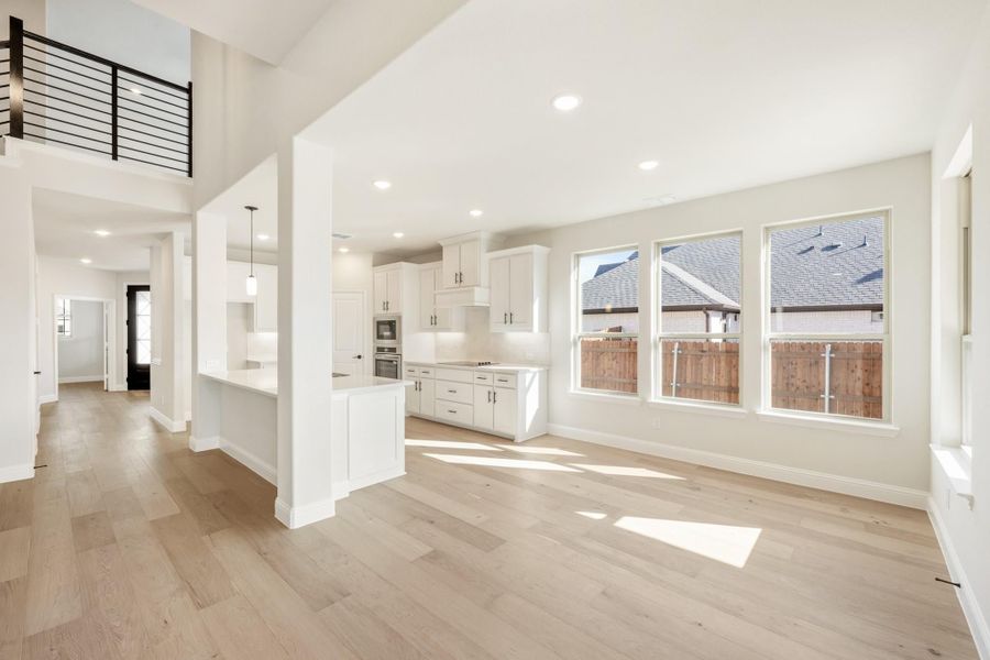Open-concept living area with light hardwood floors, white kitchen cabinets, and second-floor railing visible above
