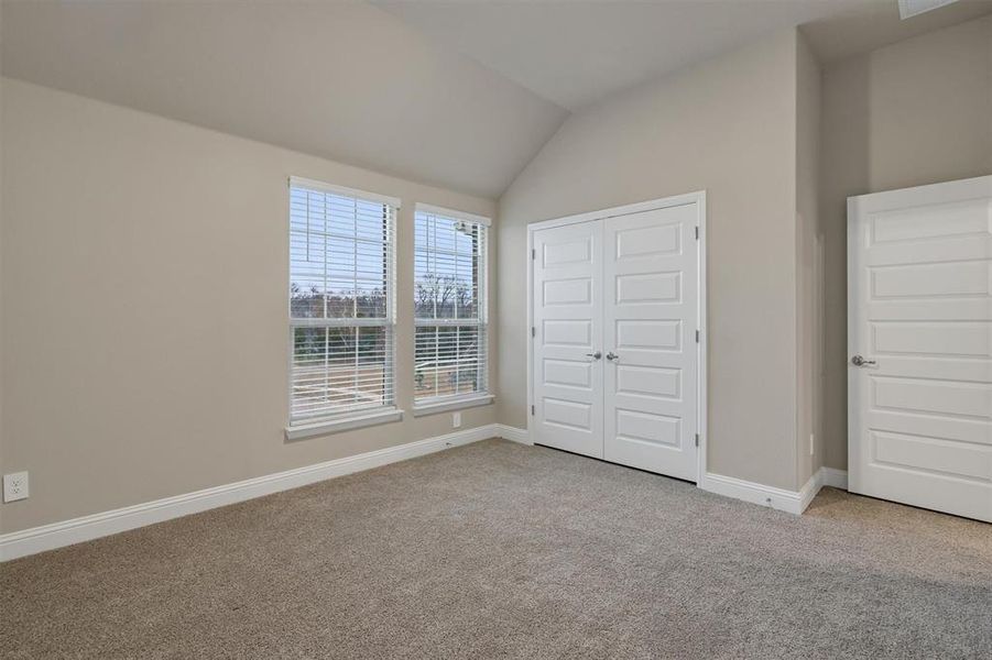 Unfurnished bedroom featuring light colored carpet, a closet, and lofted ceiling