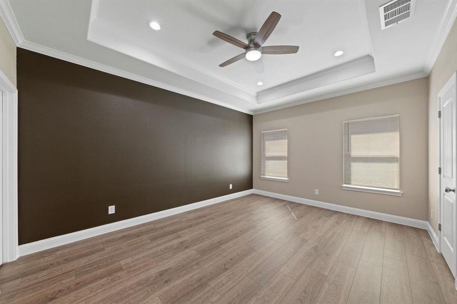 Spare room with wood finished floors, visible vents, baseboards, a raised ceiling, and crown molding