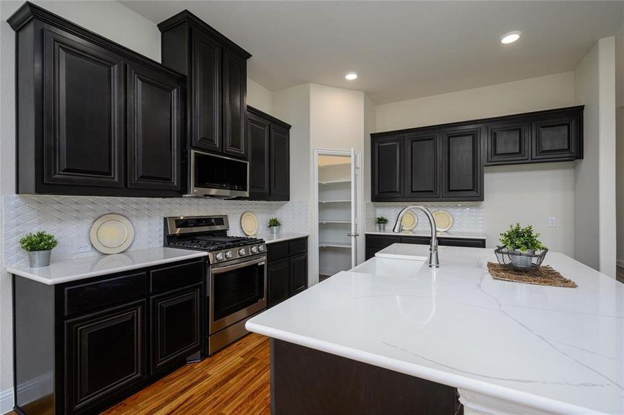 Kitchen featuring a kitchen island with sink, stainless steel appliances, hardwood / wood-style floors, decorative backsplash, and sink