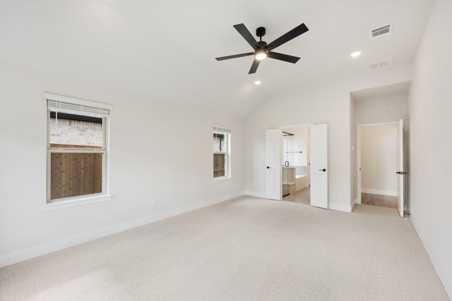 Empty bedroom with vaulted ceiling, black ceiling fan, carpet flooring, and doors leading to ensuite bathroom and closet
