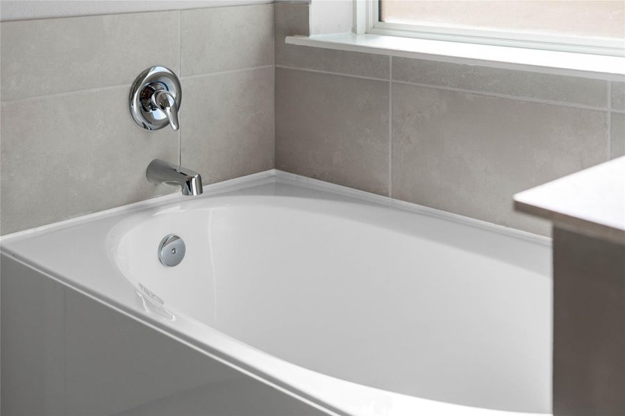 Indulge in the primary bath's deep, built-in soaking tub with elegant chrome fixtures and a sleek tile surround for a true spa-like retreat.