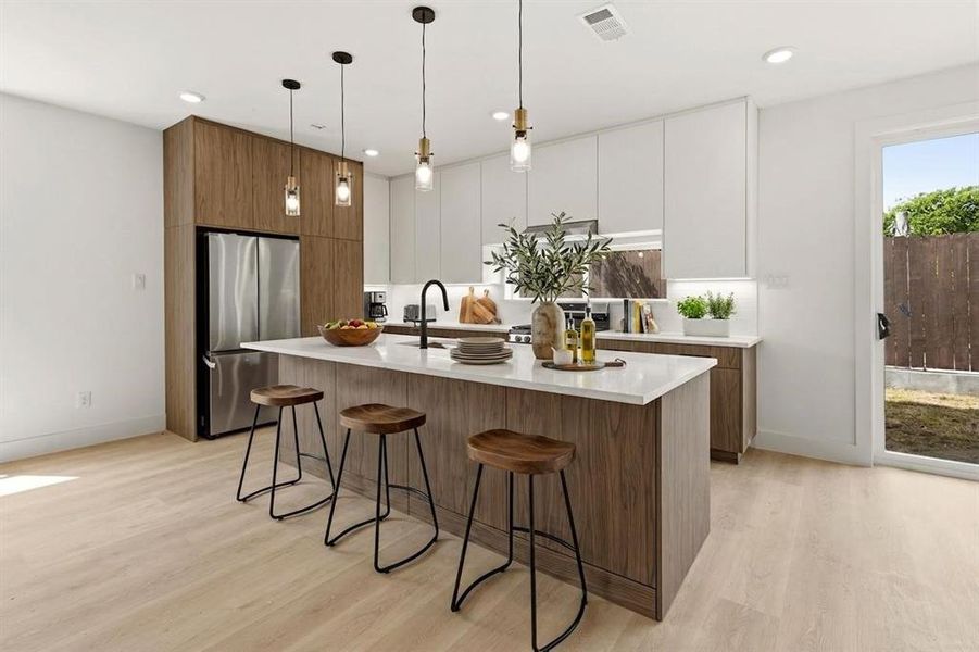 Modern kitchen featuring a large island with seating, a stainless steel refrigerator, and recessed lighting