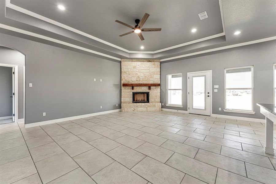 Unfurnished living room with ceiling fan, a tray ceiling, a fireplace, light tile patterned floors, and ornamental molding