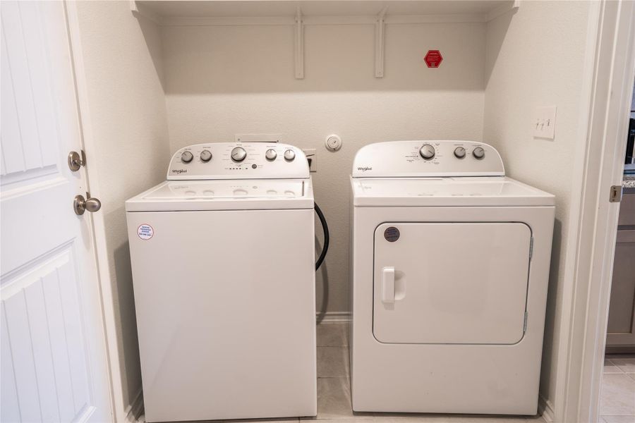 Dedicated laundry area featuring a washer and dryer, tile flooring, and overhead shelving Dedicated laundry area featuring a washer and dryer, tile flooring, and overhead shelving