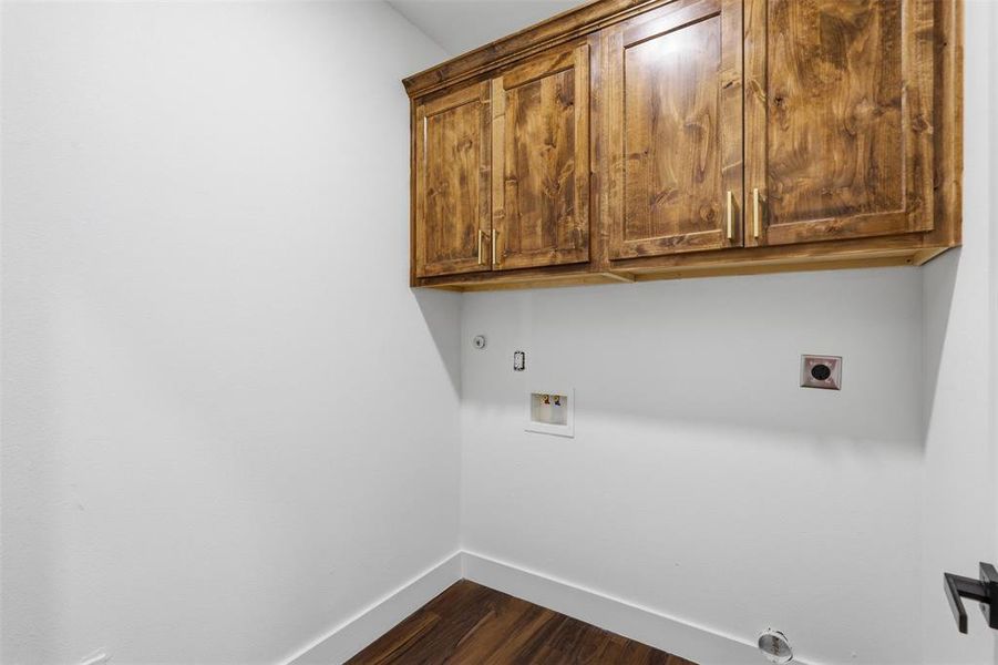Laundry room featuring rich wood cabinetry with gold-tone hardware, wood-finish flooring, and white baseboards Laundry room featuring rich wood cabinetry with gold-tone hardware, wood-finish flooring, and white baseboards