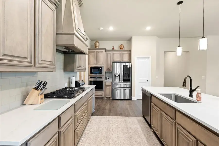 Gourmet kitchen featuring a built-in gas range, stainless steel appliances, a center island with undermount sink, pendant lighting, and wood-finish flooring Gourmet kitchen featuring a built-in gas range, stainless steel appliances, a center island with undermount sink, pendant lighting, and wood-finish flooring