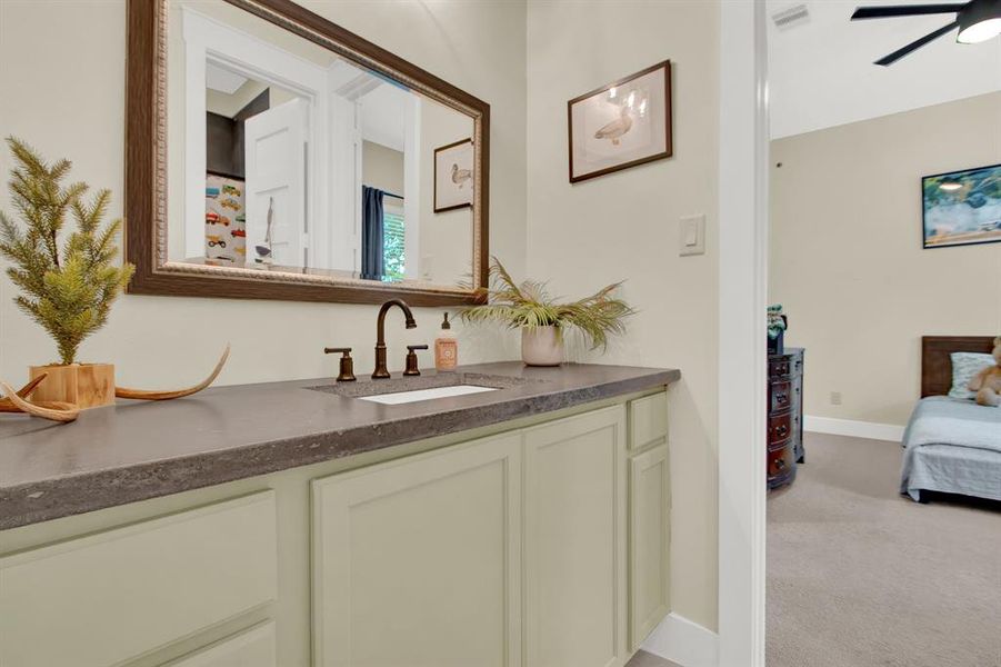 The jack-and-jill bathroom with a large mirror, undermount sink with dark countertops, and sage green cabinetry is shared by the two secondary bedrooms..