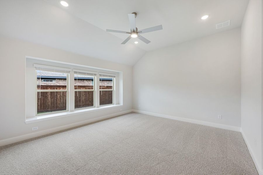 Empty bedroom with vaulted ceiling, ceiling fan, carpet flooring, and triple window with backyard view Empty bedroom with vaulted ceiling, ceiling fan, carpet flooring, and triple window with backyard view