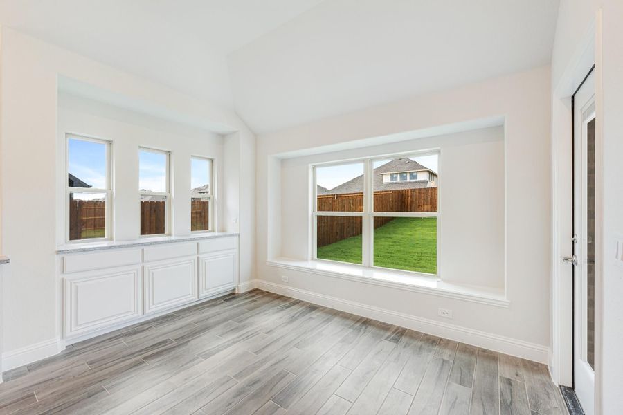 Bright empty dining room with large windows, white built-in cabinets, and wood-look tile floors overlooking a backyard