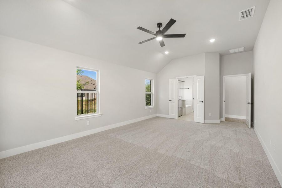 Spacious bedroom with vaulted ceiling, ceiling fan, carpet flooring, and open doors to bathroom and closet.