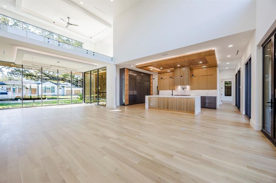 Unfurnished living room featuring light wood finished floors, recessed lighting, a towering ceiling, and a ceiling fan Unfurnished living room featuring light wood finished floors, recessed lighting, a towering ceiling, and a ceiling fan