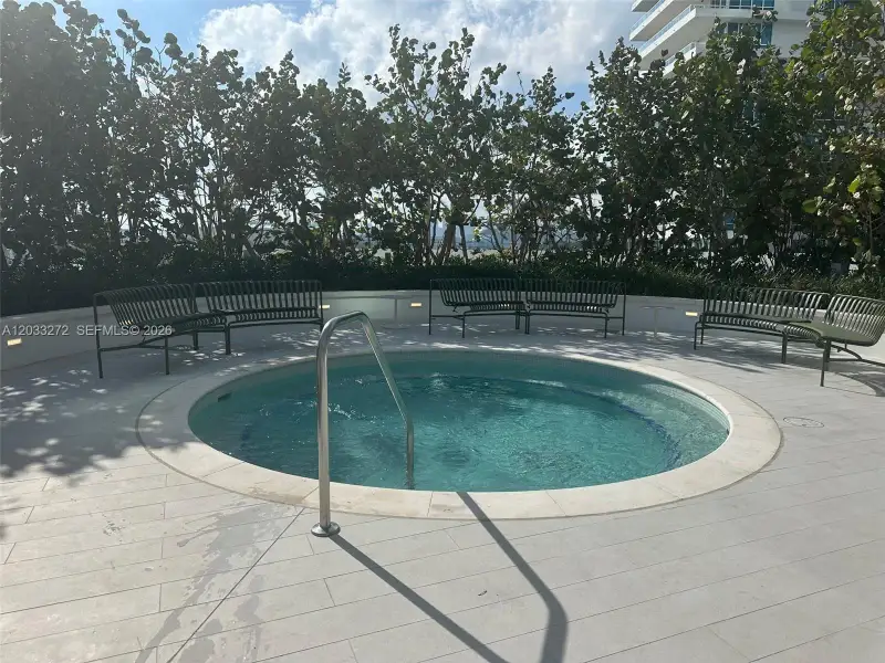 Circular spa featuring a stone coping edge, metallic handrail, perimeter landscape screening, and stone tile decking with integrated low-voltage lighting Circular spa featuring a stone coping edge, metallic handrail, perimeter landscape screening, and stone tile decking with integrated low-voltage lighting