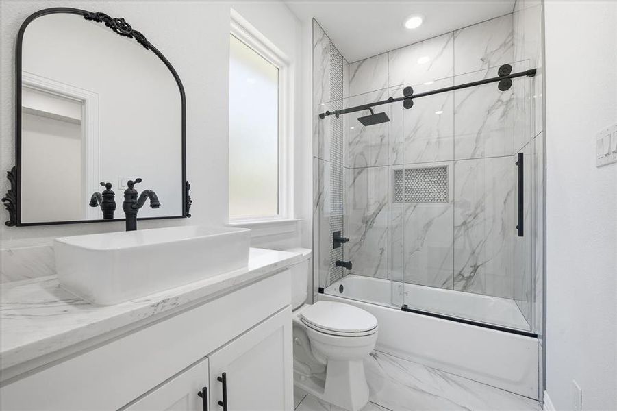Full bath featuring vanity, bath / shower combo with glass door, and marble look tiles