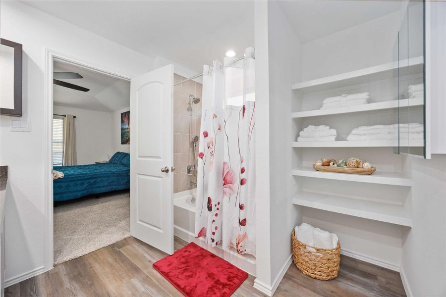 Primary Bath:Tub/shower combo with tile surround, open linen shelving, and convenient access from the primary bedroom. Primary Bath:Tub/shower combo with tile surround, open linen shelving, and convenient access from the primary bedroom.