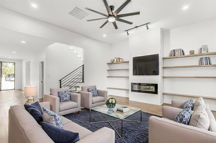 Living area featuring rail lighting, a ceiling fan, wood finished floors, stairs, and a glass covered fireplace
