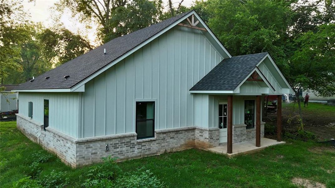 Back of property featuring a shingled roof, board and batten siding, and a yard