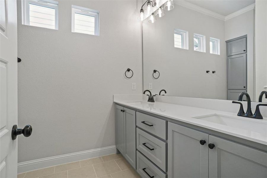 Bathroom with dual vanity, tile patterned floors, crown molding, and a wealth of natural light