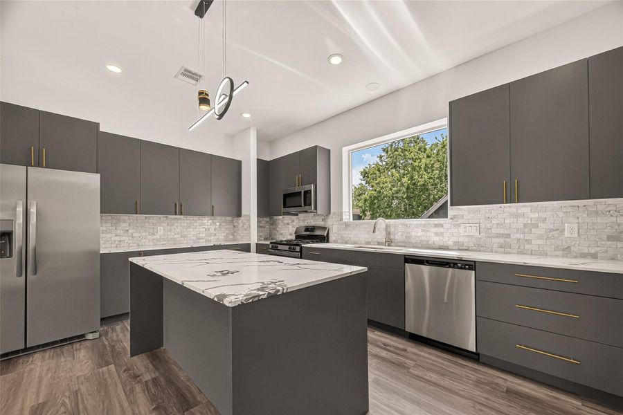 This modern kitchen features sleek gray cabinetry, a marble-patterned island, stainless steel appliances, and a large window providing natural light. The vinyl floors and stylish lighting add a contemporary touch. This modern kitchen features sleek gray cabinetry, a marble-patterned island, stainless steel appliances, and a large window providing natural light. The vinyl floors and stylish lighting add a contemporary touch.