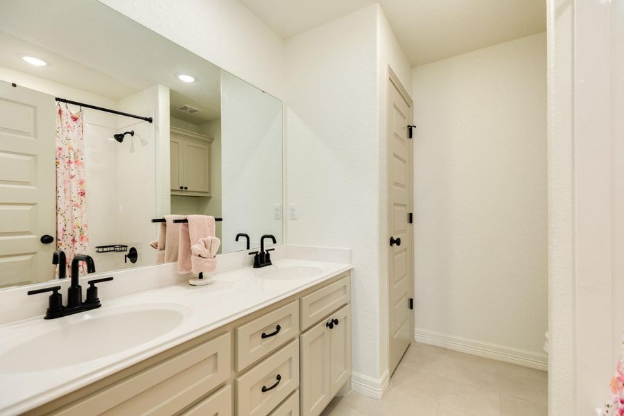 This bathroom features a double vanity with black fixtures, a large mirror, and a shower with a floral curtain. The space is bright and modern with ample storage.