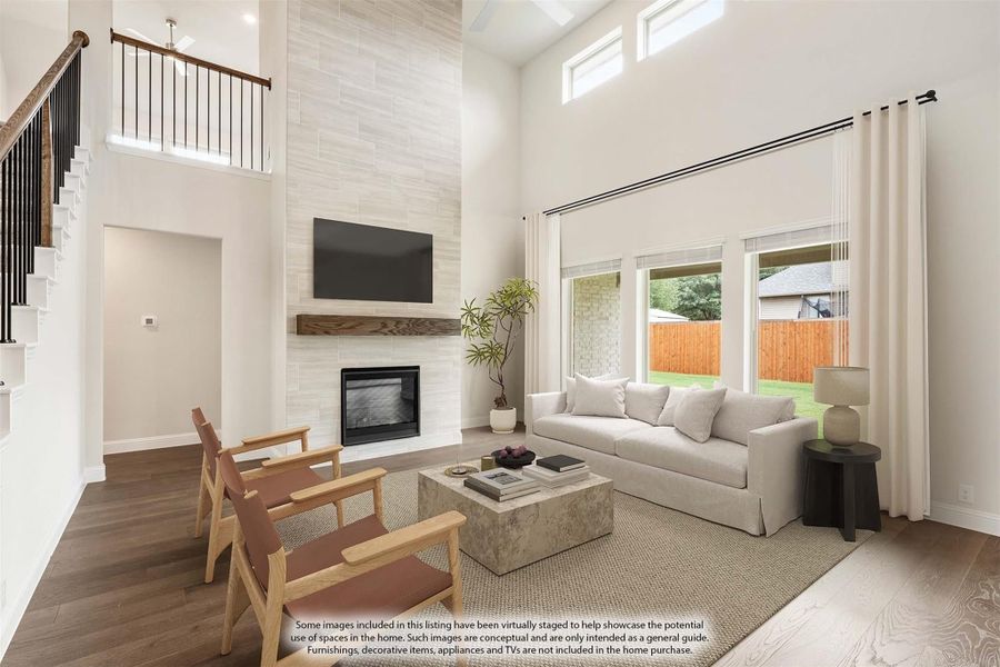 Living room with two-story ceiling, tile fireplace wall, hardwood floors, and large windows overlooking backyard