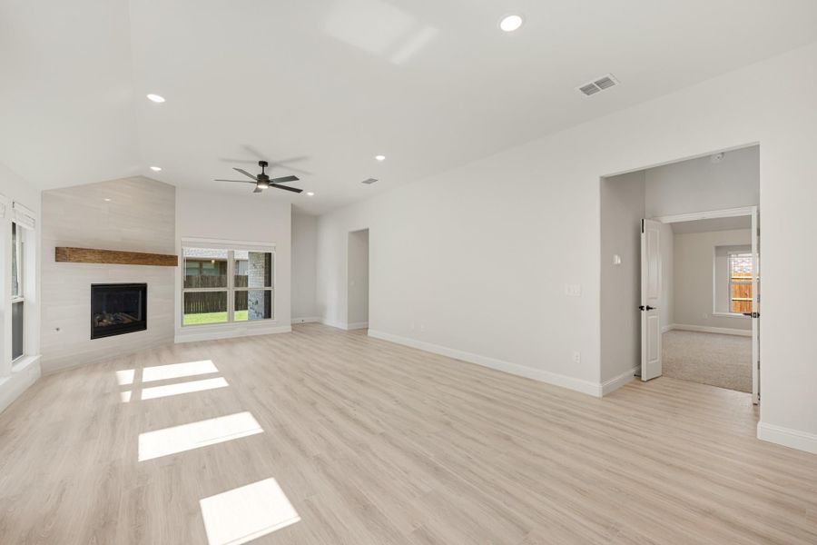 Open living room with light wood floors, ceiling fan, and fireplace with wood mantel