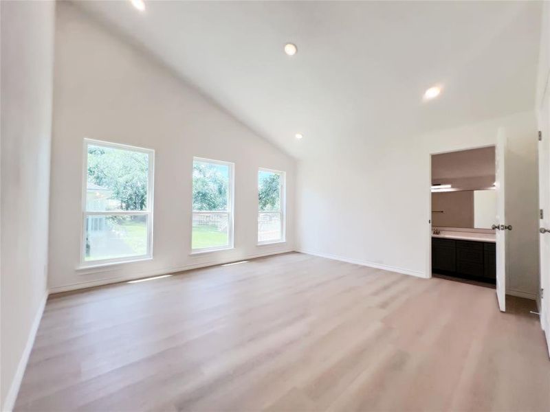 Spacious room featuring a vaulted ceiling with recessed lighting, three large windows, light wood-finish flooring, and white walls