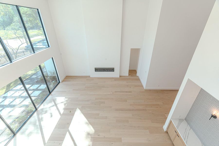 This spacious living area features high ceilings and large windows that flood the room with natural light. The light wood flooring and modern design elements create an airy and inviting atmosphere.