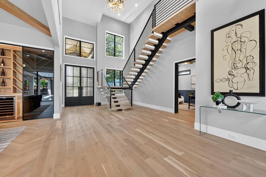 Two-story foyer featuring light wood-finish flooring, a modern floating staircase with metal railings, and a built-in beverage bar with a wine cooler Two-story foyer featuring light wood-finish flooring, a modern floating staircase with metal railings, and a built-in beverage bar with a wine cooler