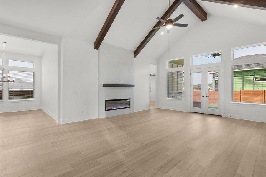 Unfurnished living room with high vaulted ceiling, a large fireplace, beamed ceiling, light wood-style flooring, and a chandelier