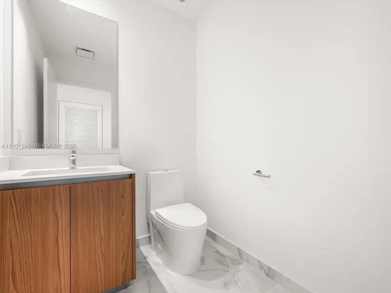 Wood-finish vanity cabinet, solid-surface countertop with integrated sink, chrome faucet, large rectangular wall mirror, and neutral tile flooring Wood-finish vanity cabinet, solid-surface countertop with integrated sink, chrome faucet, large rectangular wall mirror, and neutral tile flooring