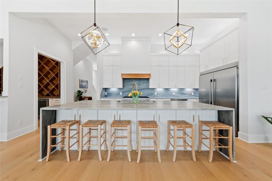 Crafted for entertaining, the chef's kitchen showcases an expansive waterfall island with seating, custom cabinetry, premium appliances, a dramatic stone backsplash, and abundant prep space for hosting family and friends. Crafted for entertaining, the chef's kitchen showcases an expansive waterfall island with seating, custom cabinetry, premium appliances, a dramatic stone backsplash, and abundant prep space for hosting family and friends.