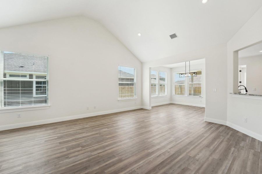 Living room with wood-style vinyl flooring, visible vents, baseboards, a chandelier, and high vaulted ceiling Living room with wood-style vinyl flooring, visible vents, baseboards, a chandelier, and high vaulted ceiling