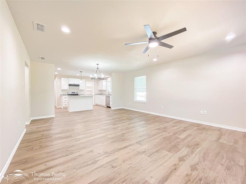 Unfurnished living room featuring recessed lighting, light wood-type flooring, ceiling fan, and a chandelier Unfurnished living room featuring recessed lighting, light wood-type flooring, ceiling fan, and a chandelier