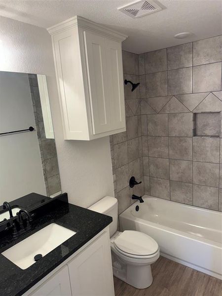 Full bathroom featuring hardwood / wood-style floors, a textured ceiling, tiled shower / bath, vanity, and toilet