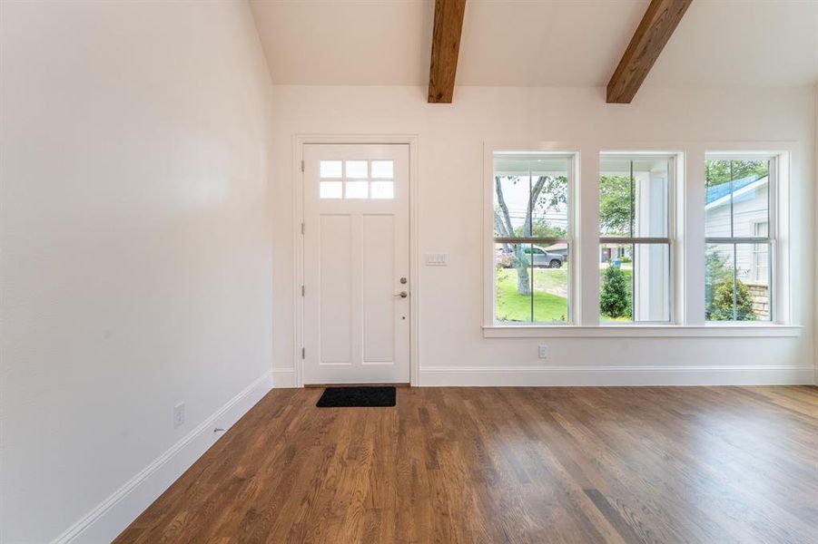 Entryway featuring a paneled door with glass inserts, wood-finish flooring, three vertical windows, white trim, and exposed ceiling beams Entryway featuring a paneled door with glass inserts, wood-finish flooring, three vertical windows, white trim, and exposed ceiling beams