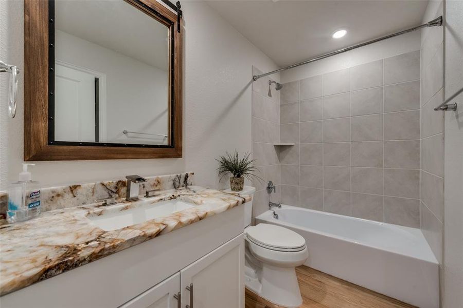 Full bathroom featuring exotic granite counter top oversized vanity, designer LED faucet, custom mirror, tiled shower / bath combo, toilet, and wood flooring