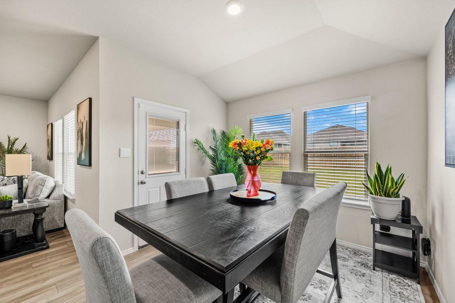 Natural light floods this dining area, featuring vaulted ceilings and durable wood-look flooring.