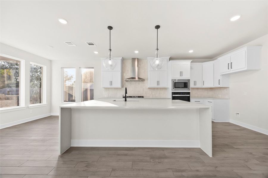 This photo showcases a modern kitchen with a spacious open layout. It features sleek white cabinetry, a large center island with a sink, pendant lighting, and stainless steel appliances. Large windows provide ample natural light, highlighting the wood-look porcelain tile flooring. This photo showcases a modern kitchen with a spacious open layout. It features sleek white cabinetry, a large center island with a sink, pendant lighting, and stainless steel appliances. Large windows provide ample natural light, highlighting the wood-look porcelain tile flooring.