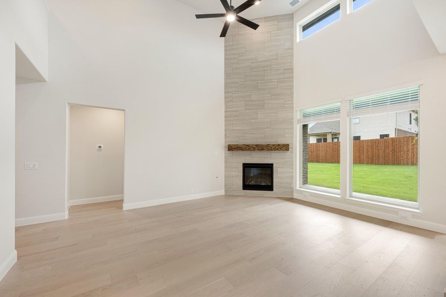 Open living room with vaulted ceiling, floor-to-ceiling tile fireplace, hardwood floors, and large windows overlooking backyard Open living room with vaulted ceiling, floor-to-ceiling tile fireplace, hardwood floors, and large windows overlooking backyard