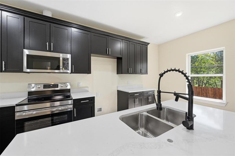 Kitchen featuring stainless steel appliances, dark cabinetry, light stone counters, and recessed lighting Kitchen featuring stainless steel appliances, dark cabinetry, light stone counters, and recessed lighting